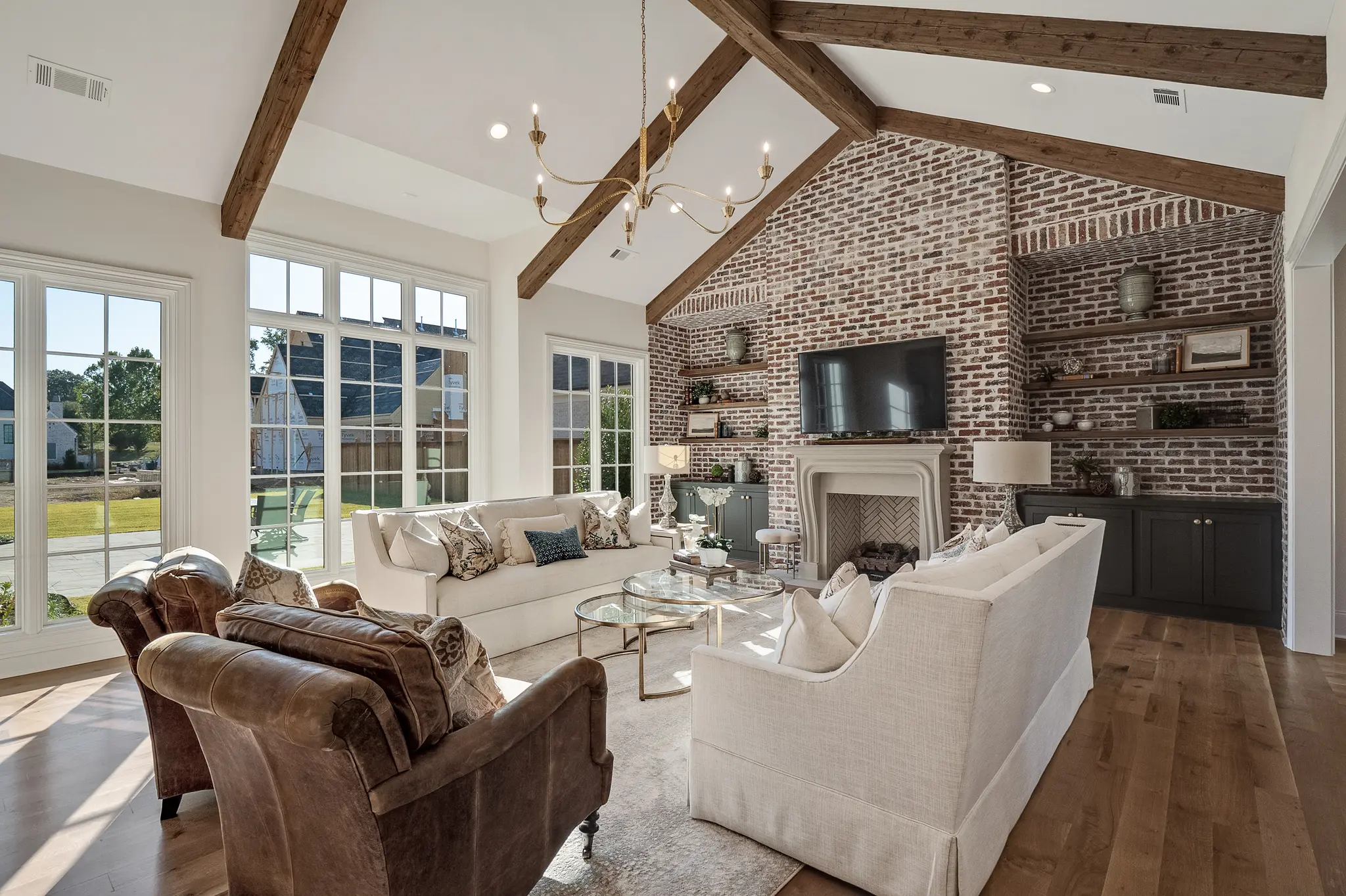 Family Room with gorgeous furniture, stunning brick fireplace with limestone mantle, vaulted ceilings with cedar beams, and luxurious open-shelves built-ins!