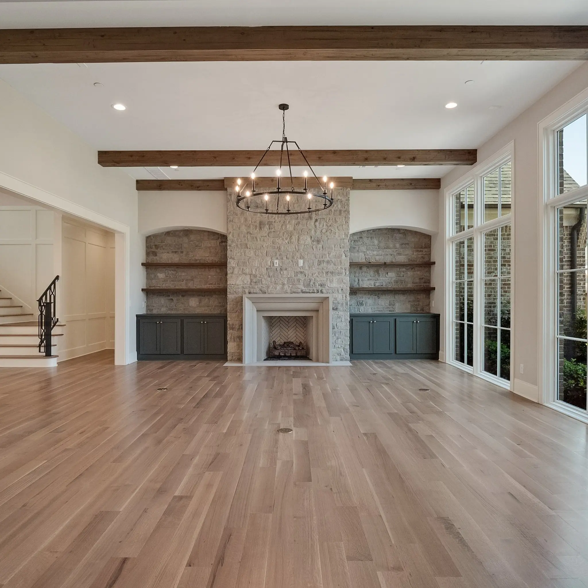 Quality craftsmanship displayed through a family room with stone fireplace, open shelving built-ins, green base cabinets, cedar floating shelves, cedar beams, and giant windows!