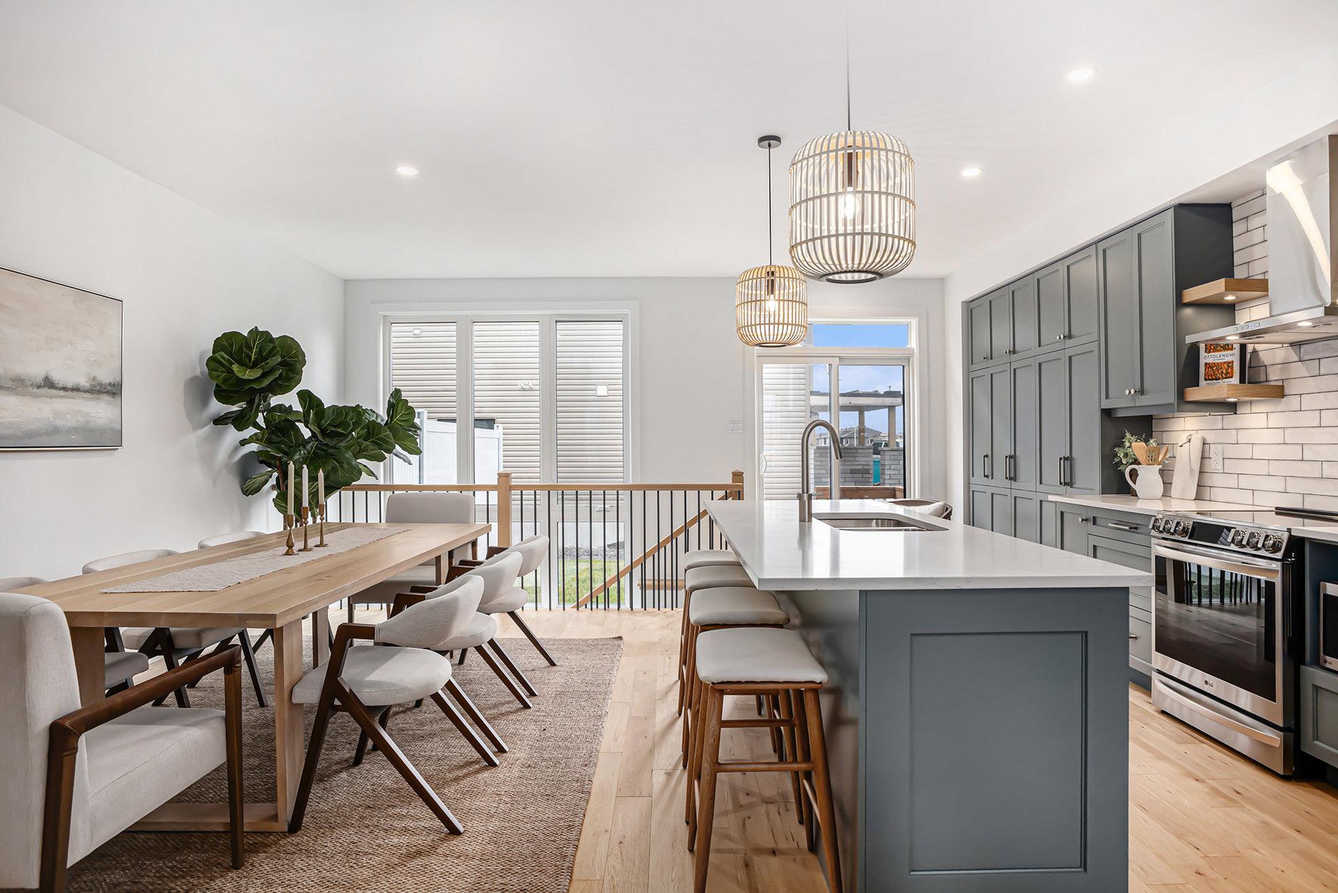 Modern kitchen and dining area with gray cabinets, white island, wood table, and pendant lighting