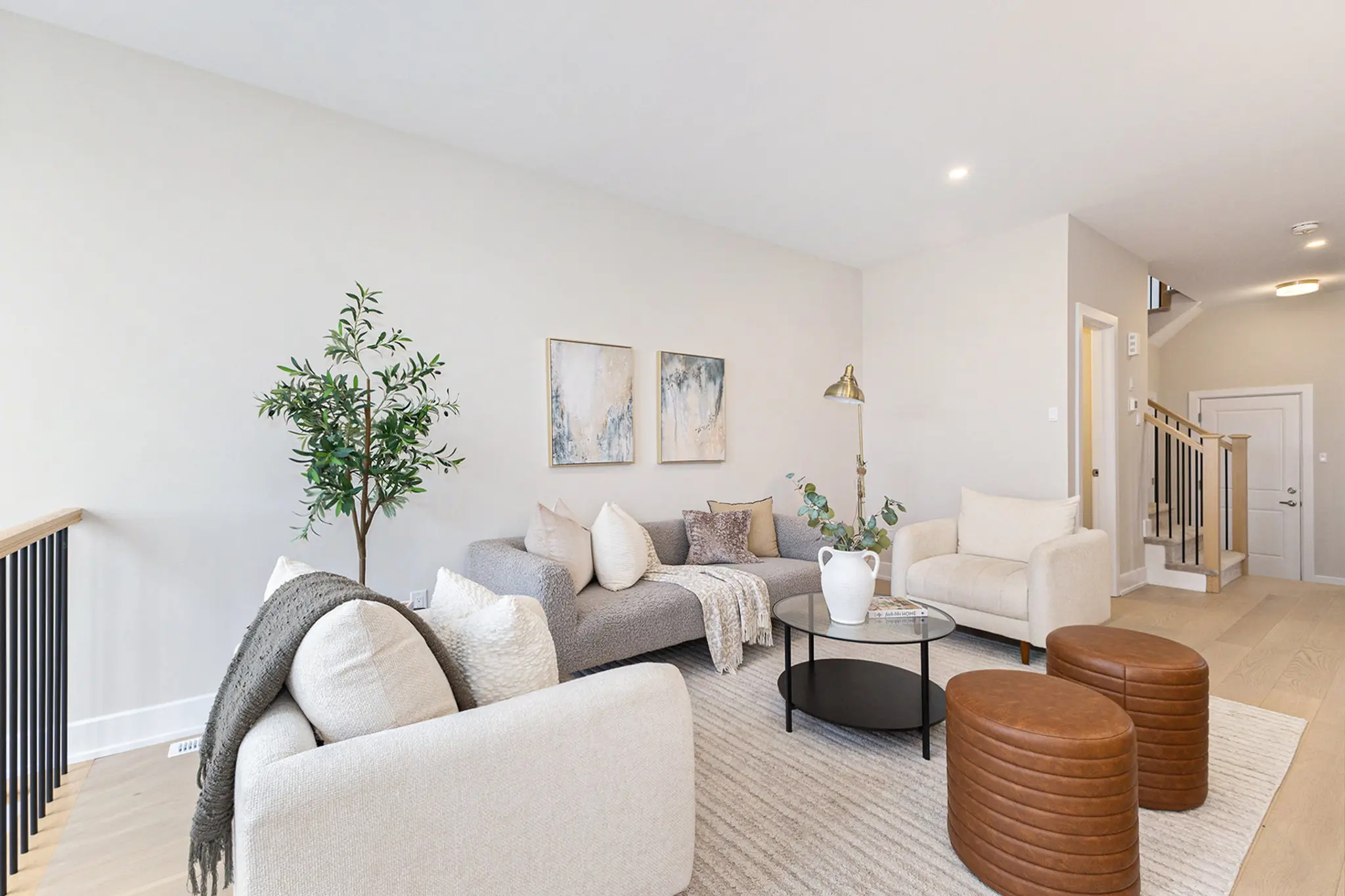 Modern living room with neutral furniture, round coffee table, indoor plant, and light wood flooring