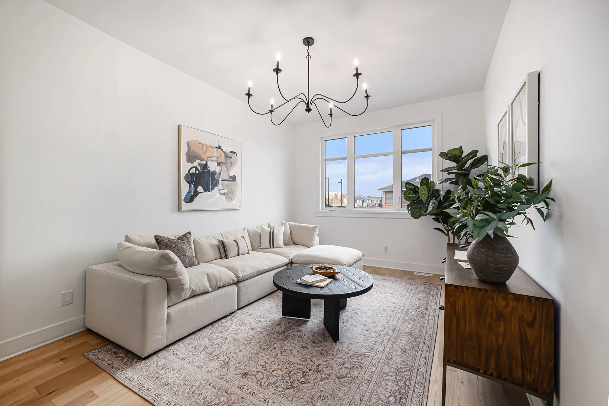 Bright modern living room with cream sectional sofa, black chandelier, and large window