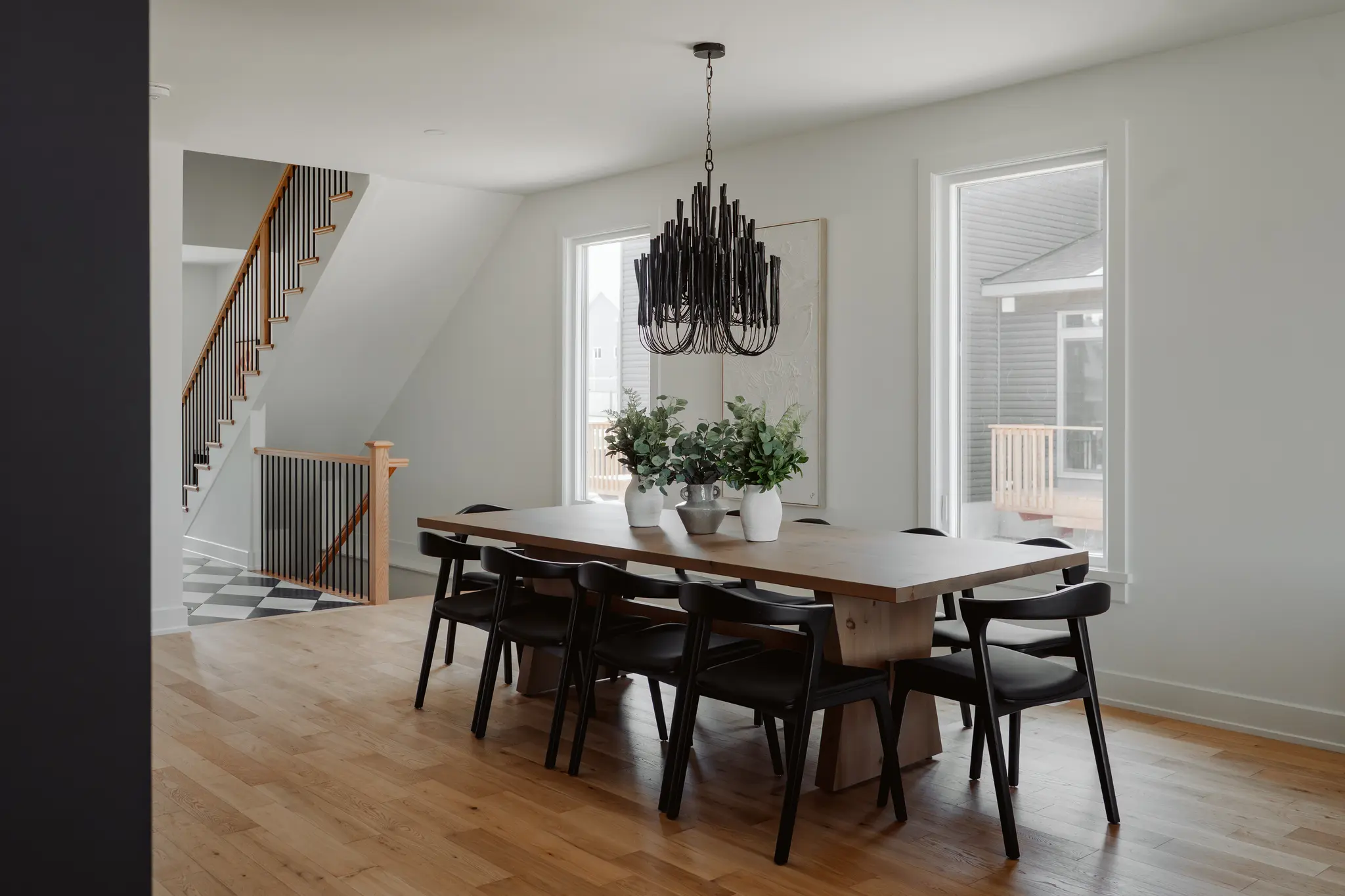 Modern dining room with wood table, black chairs, and statement chandelier beside staircase