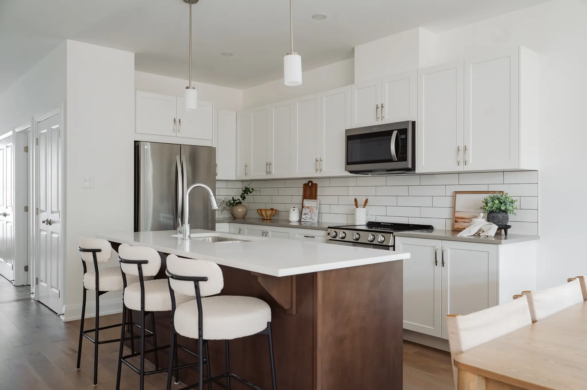 Modern white kitchen with large island, bar stools, stainless steel appliances, and subway tile backsplash