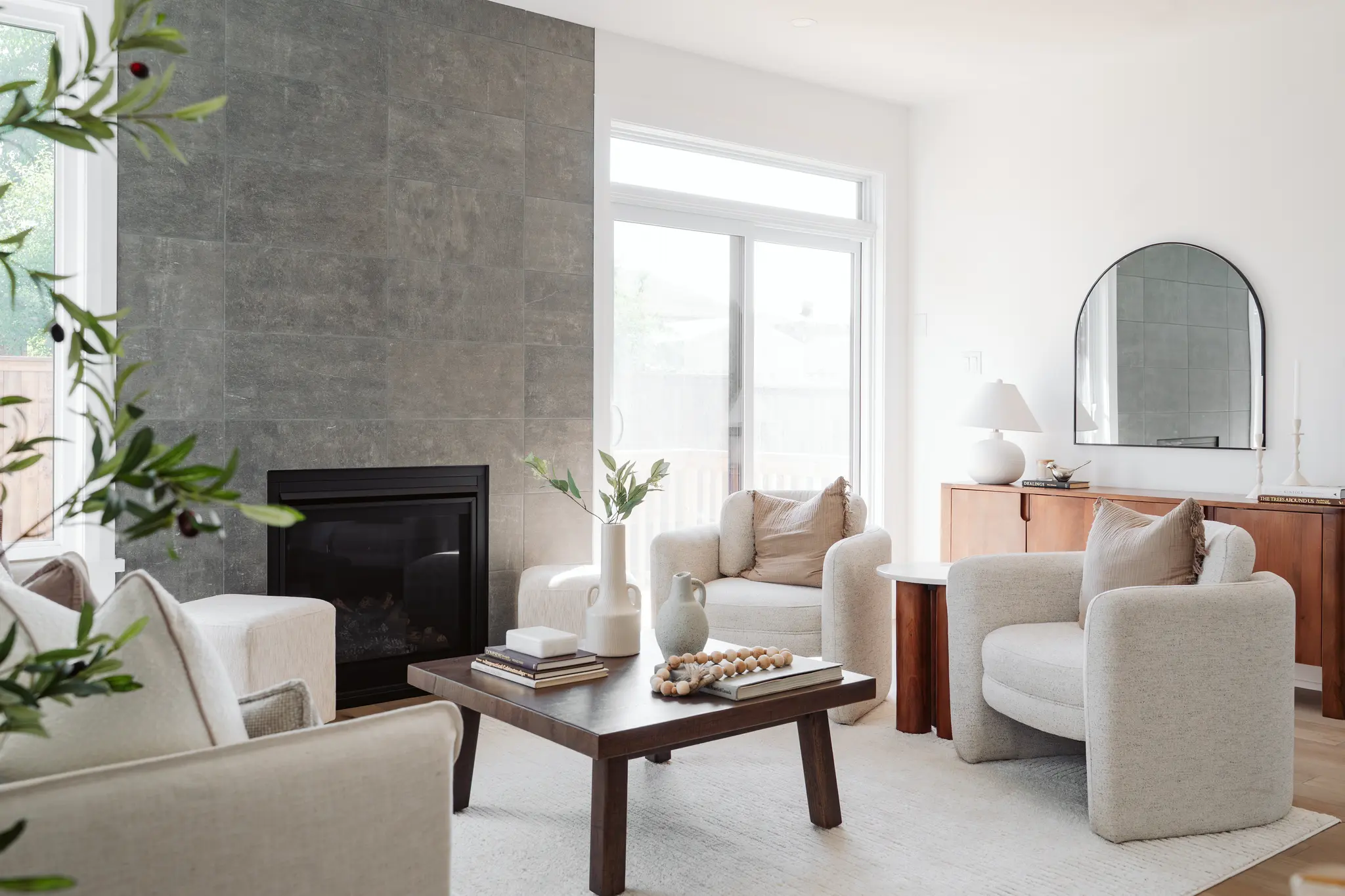 Bright living room with fireplace, cream armchairs, wood coffee table, and large windows